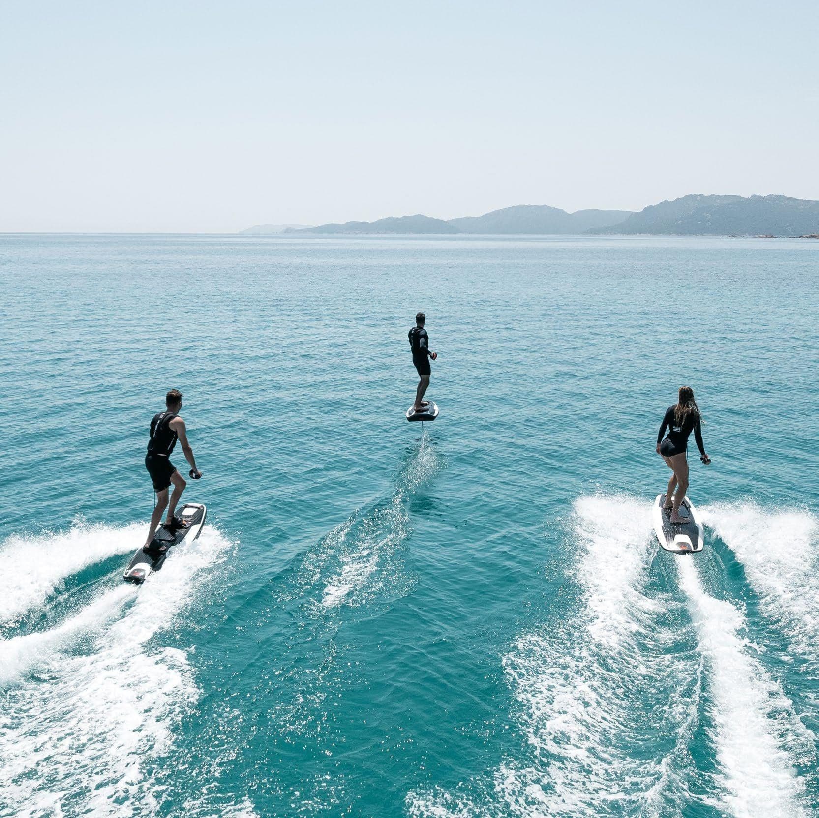 Three riders in formation on AWAKE electric surfboards across calm Mediterranean water